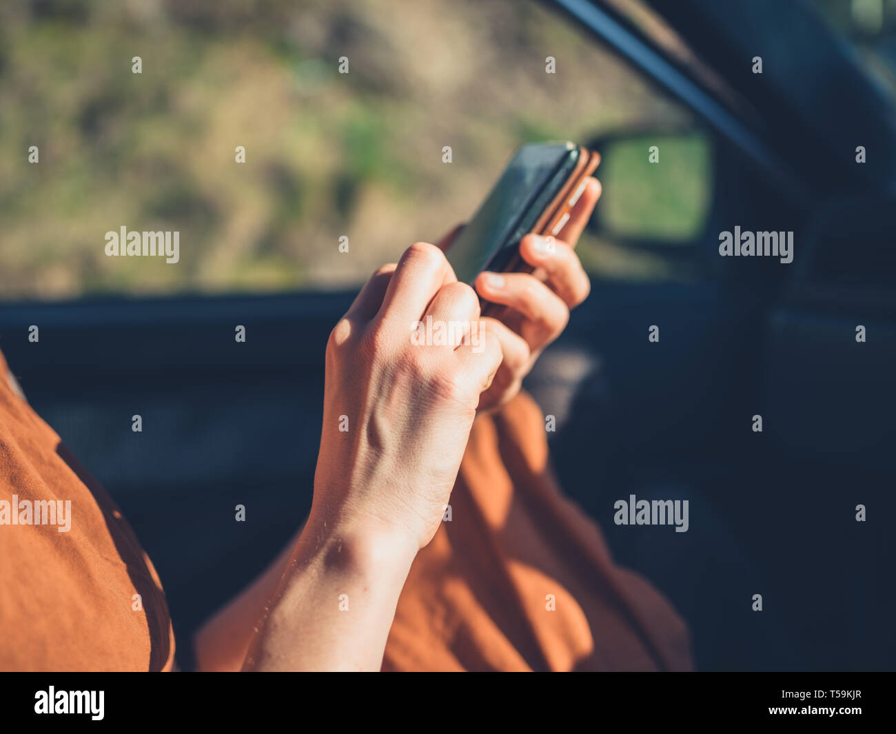 Eine junge Frau wird mit einem Smartphone in einem geparkten Auto Stockfoto