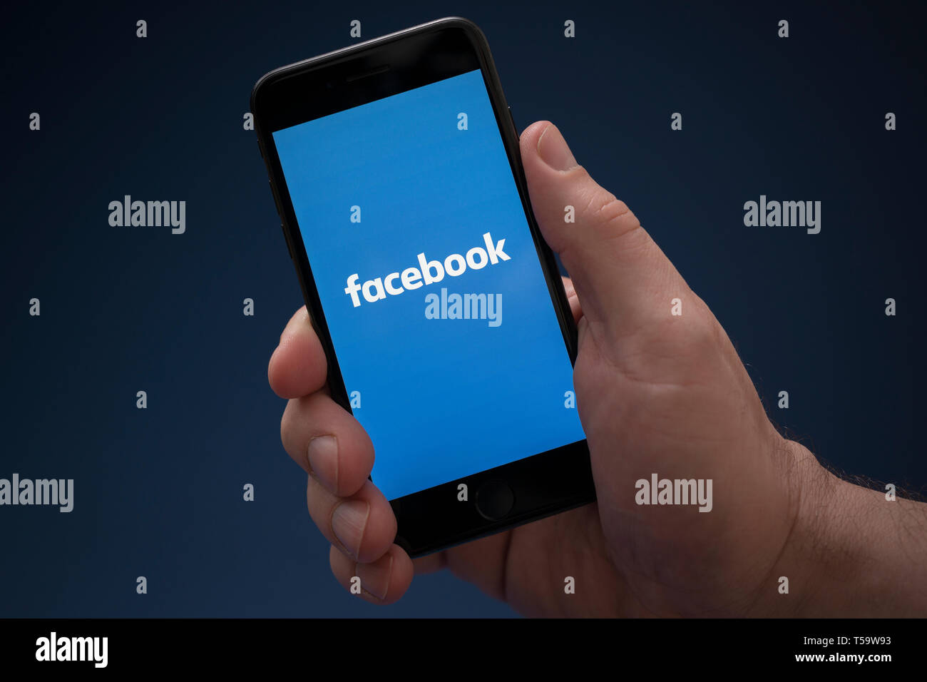 Ein Mann schaut auf seinem iPhone. das Facebook Logo (nur redaktionelle Nutzung). Stockfoto