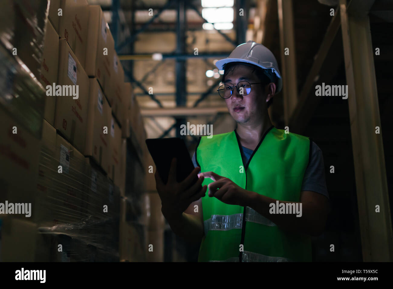 Jungen Asiatischen männliche Lagerarbeiter mit einem digitalen Tablet in Lager und Lagerverwaltung in der Fabrik zu prüfen. Stockfoto