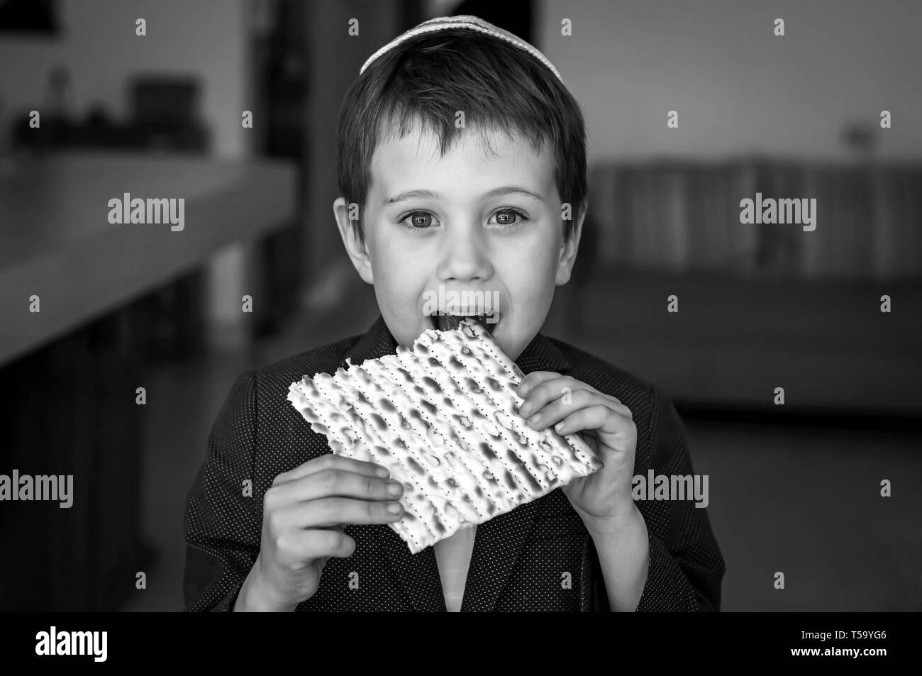 Cute kaukasischen Kind in einer Kippa, einen Bissen von einem traditionellen jüdischen matzo ungesäuertes Brot in einem Raum. Schwarz-weiß-Bild. Stockfoto