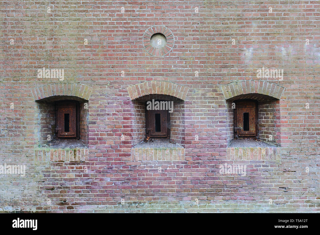 Brick Wall von einer alten Festung mit drei embresures mit rostigem Eisen Luken geschlossen. Stockfoto
