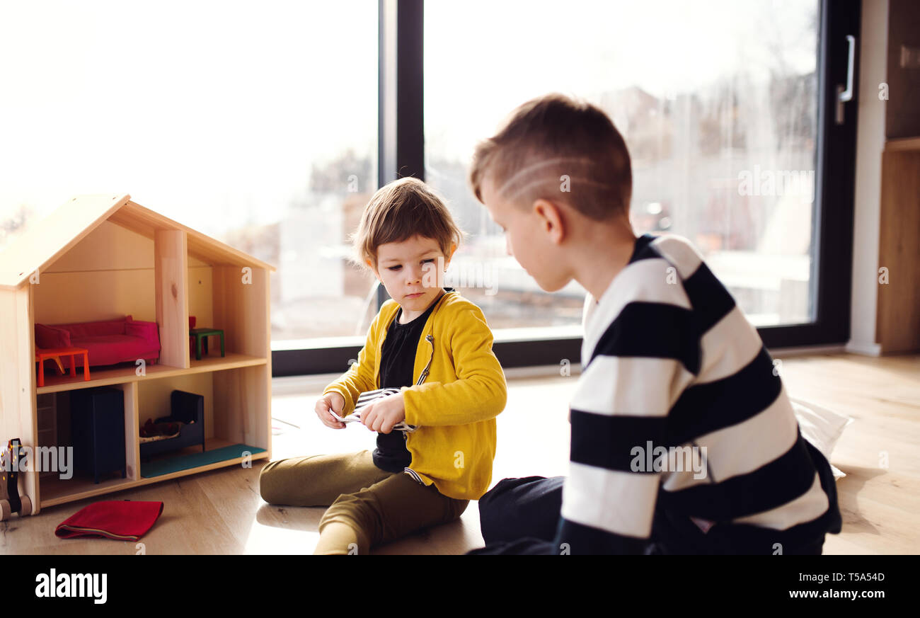 Zwei glückliche Kinder spielen mit einem Holzhaus in Innenräumen zu Hause. Stockfoto