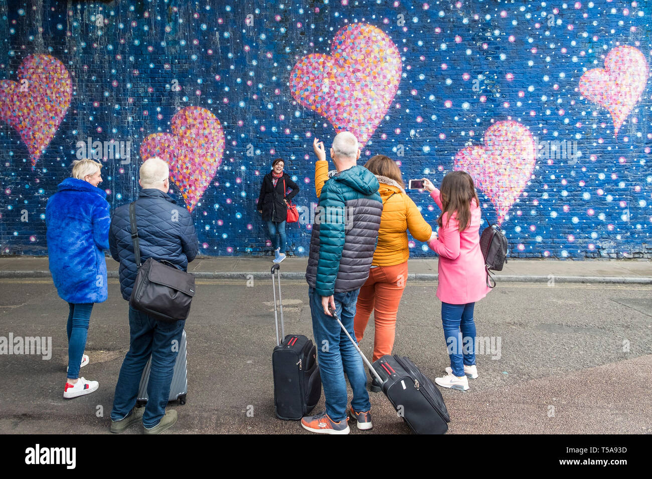 Menschen beobachten, wie Frauen vor einem großen gemalten Wandgemälde mit rosa Herzen posieren, gemalt von Jimmy C. in Erinnerung an die Terrorangriffe auf die London Bridge. Stockfoto