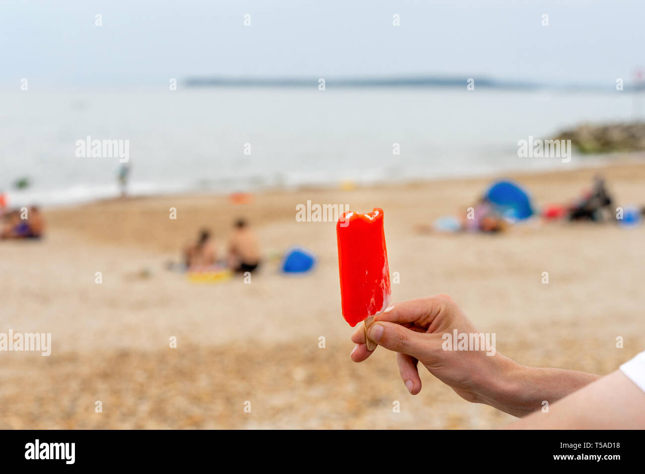 Mann hält ein rotes Eis lolly in der Hand an einem Strand in Großbritannien im Sommer Stockfoto