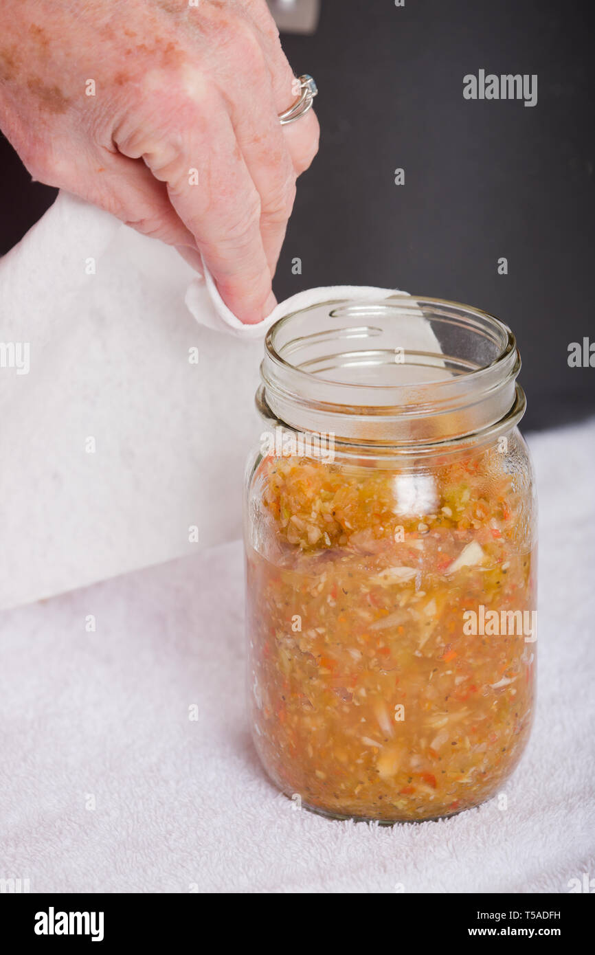 Frau Abwischen der Relish jar Rim, bevor Sie den Deckel und Ring auf, um eine gute Abdichtung zu gewährleisten. (MR) Stockfoto