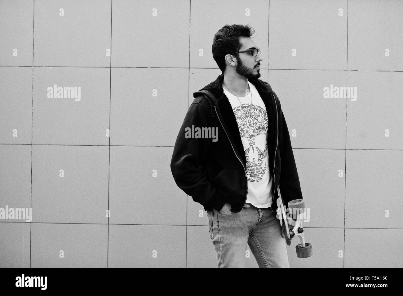 Street Style Araber in Brillen mit Longboard gegen graue Wand gestellt. Stockfoto