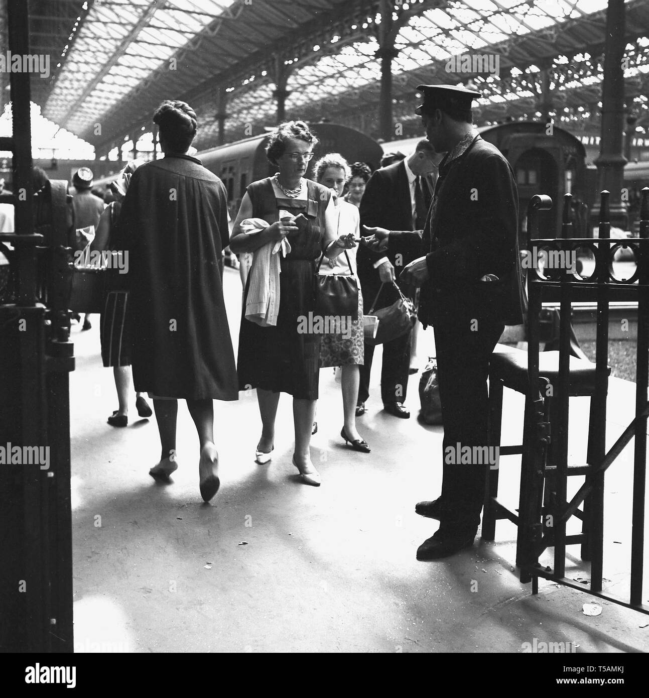 1960er Jahre, historisch, in einem Bahnhof, ein uniformierter Bahnsteig Wache oder Ticket Inspektor sammeln eine abfahrenden weiblichen Zug Fahrschein am Ausgang Gate, London Paddington. Stockfoto
