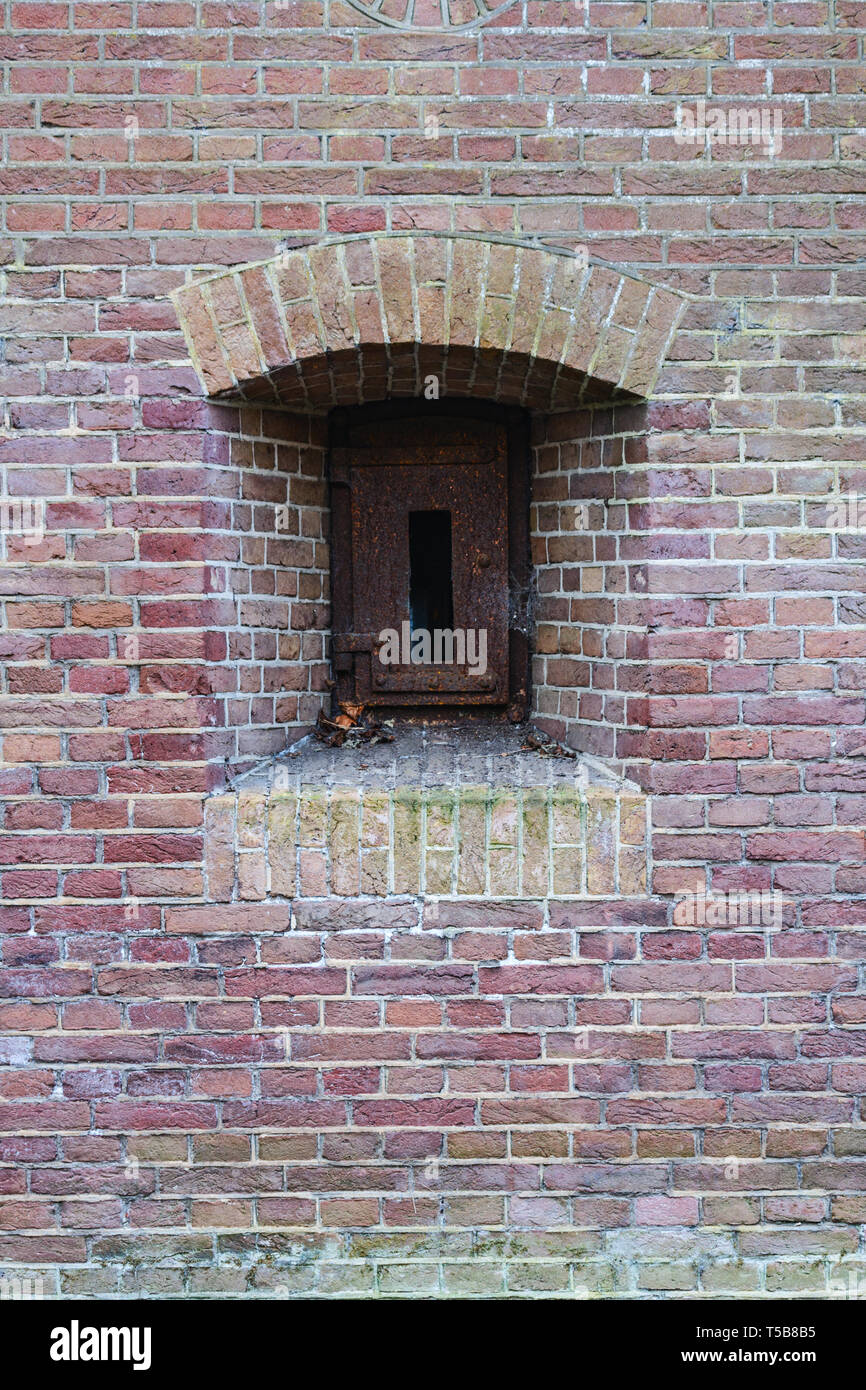 Brick Wall von einer alten Festung mit einem embresures mit rostigem Eisen Klappe geschlossen. Stockfoto