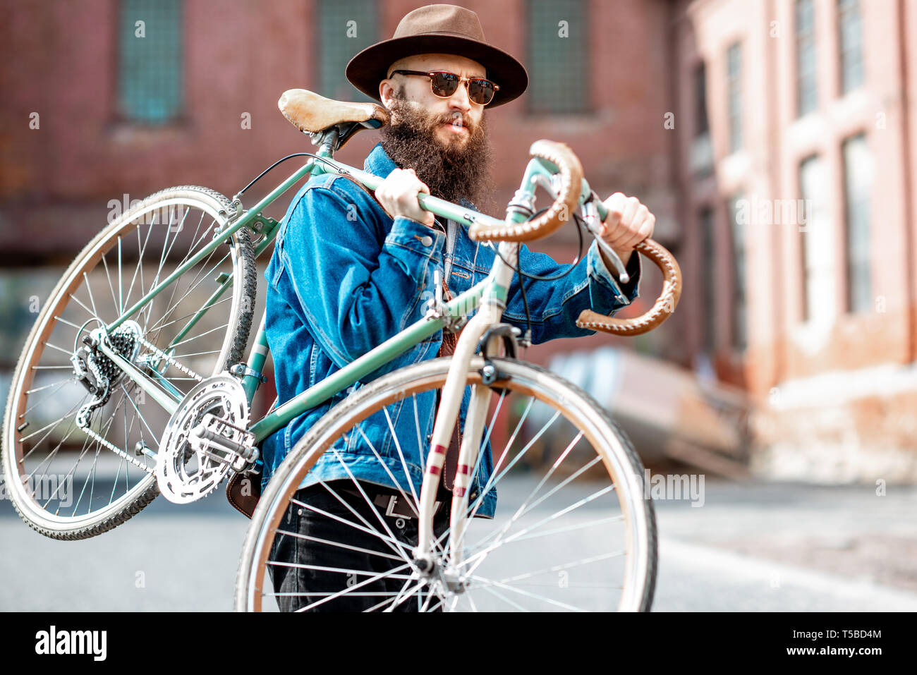 Lifestyle Portrait eines bärtigen Hipster stilvoll gekleidet mit Hut und Jacke seine retro Fahrrad auf dem städtischen Hintergrund Stockfoto