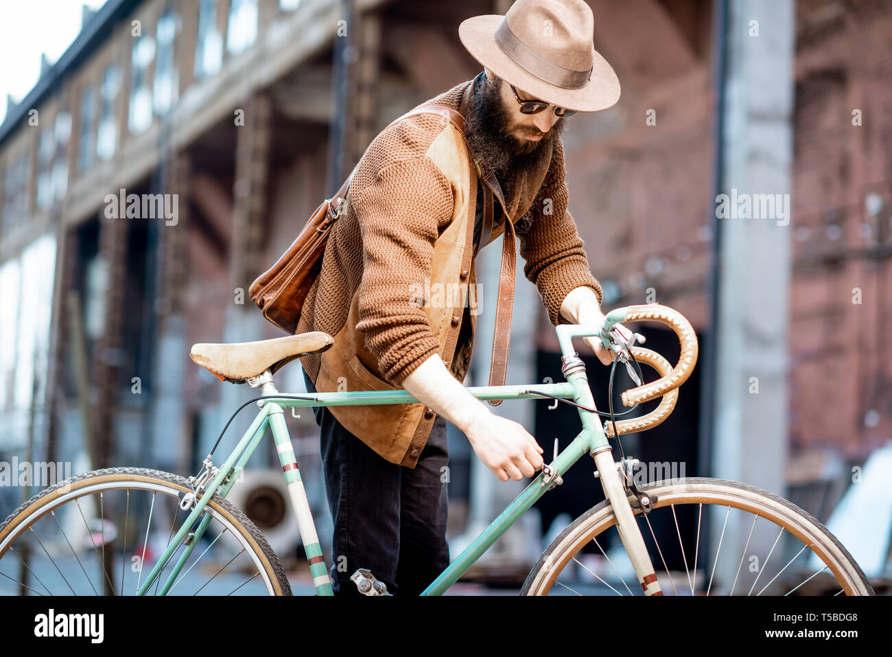 Bärtige hipster stilvoll gekleidet mit Hut stehend mit retro Fahrrad draußen auf der städtischen Hintergrund Stockfoto