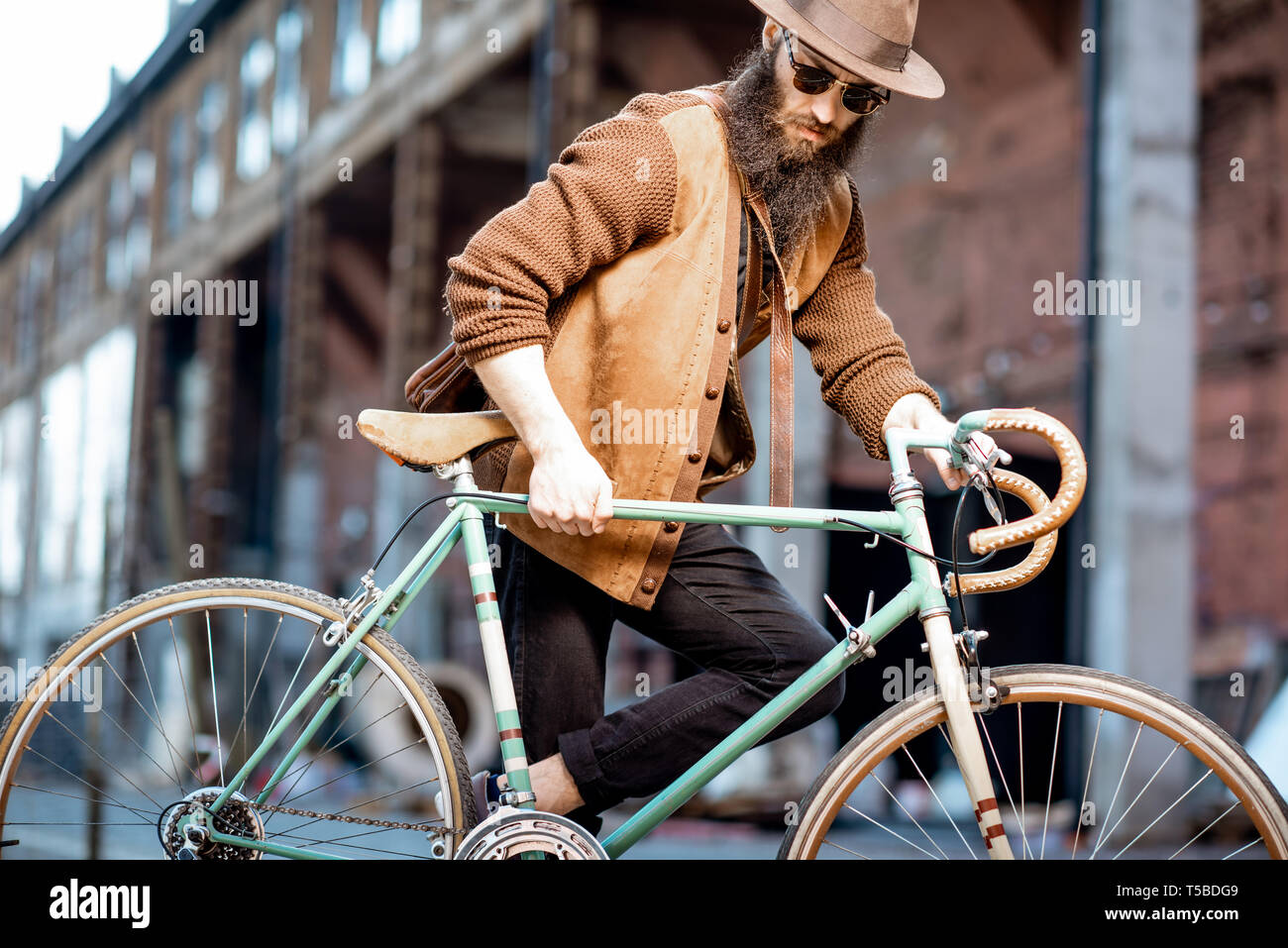 Bärtige hipster stilvoll gekleidet mit Hut stehend mit retro Fahrrad draußen auf der städtischen Hintergrund Stockfoto