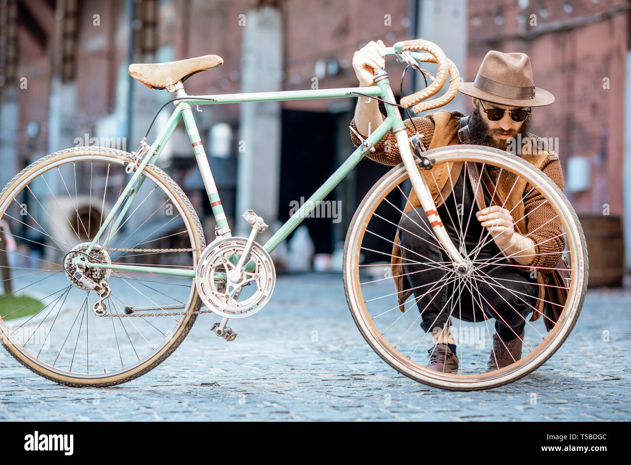 Bärtige hipster stilvoll gekleidet mit Hut stehend mit retro Fahrrad draußen auf der städtischen Hintergrund Stockfoto