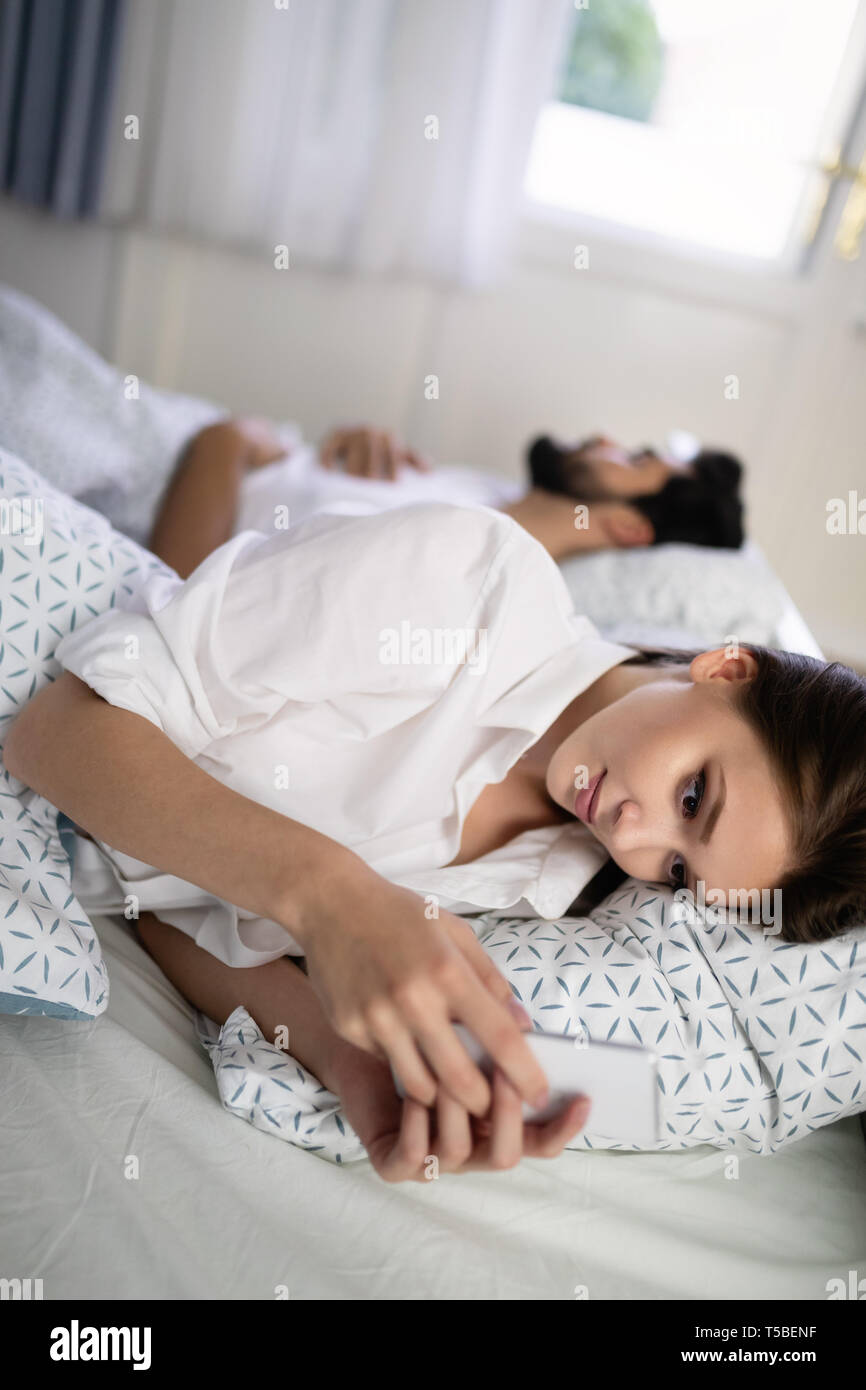 Schöne junge Frau sms mit Liebhaber auf dem Smartphone während Mann schläft Stockfoto
