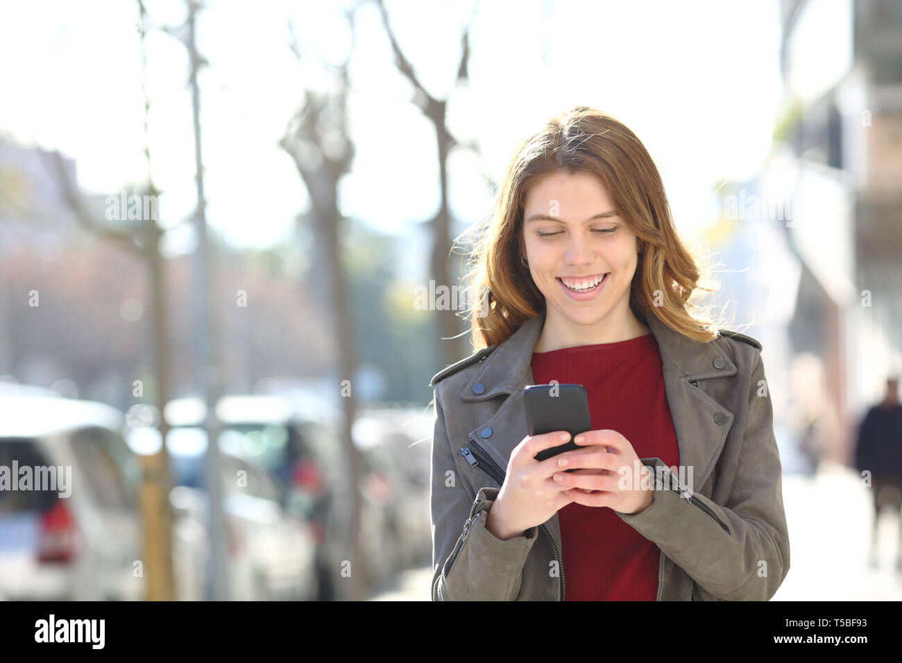 Vorderansicht Portrait Of Happy Teenager zu Fuß mit einem Smart Phone auf der Straße Stockfoto