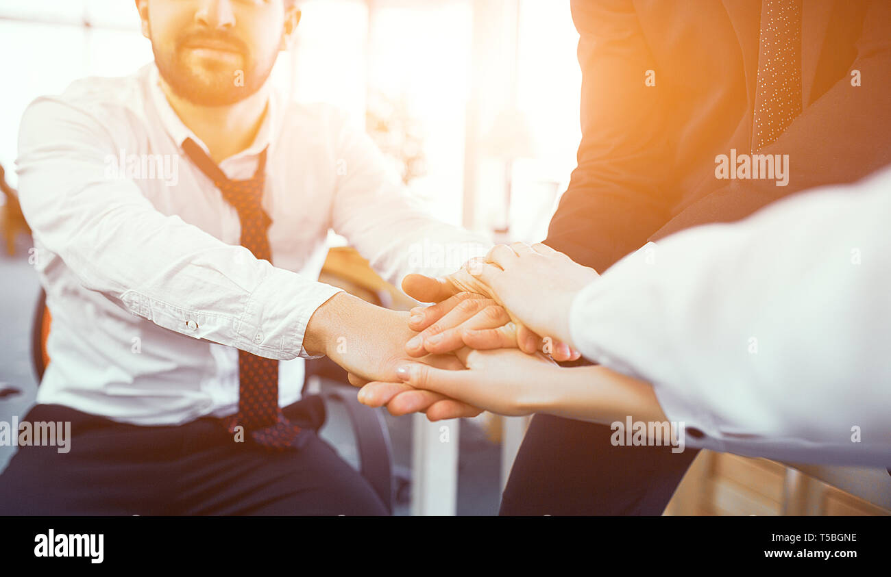 Kollegen Kreuzung Hände im Sonnenlicht in modernen Büro. Selektiver Fokus auf die Hände. Bärtige Mann auf Hintergrund. Stockfoto