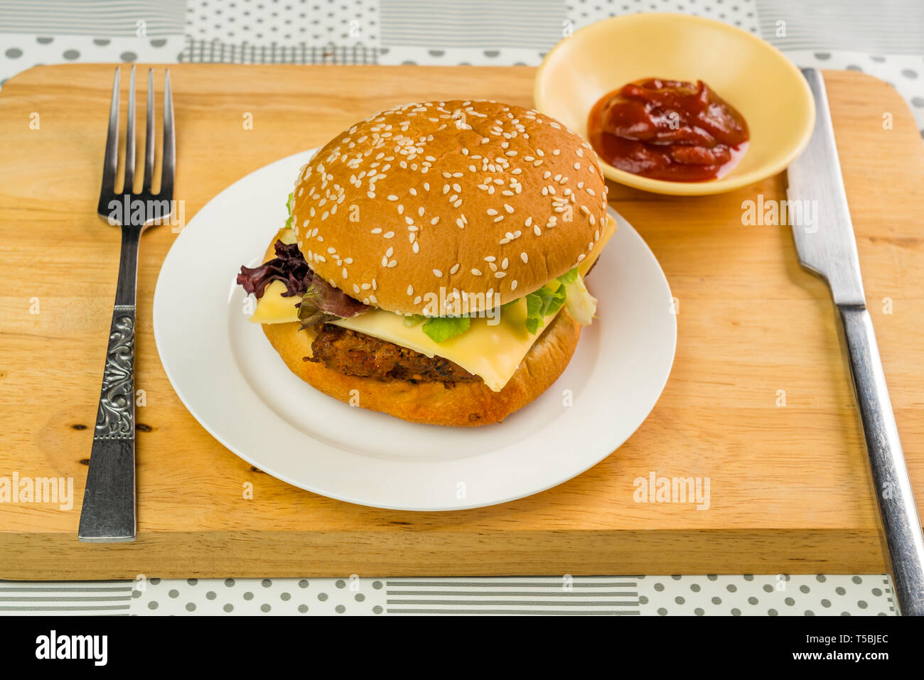 Chicken Burger mit Käse und Gemüse ist bereit, in einer weißen Platte auf Holzbrett zu essen Stockfoto