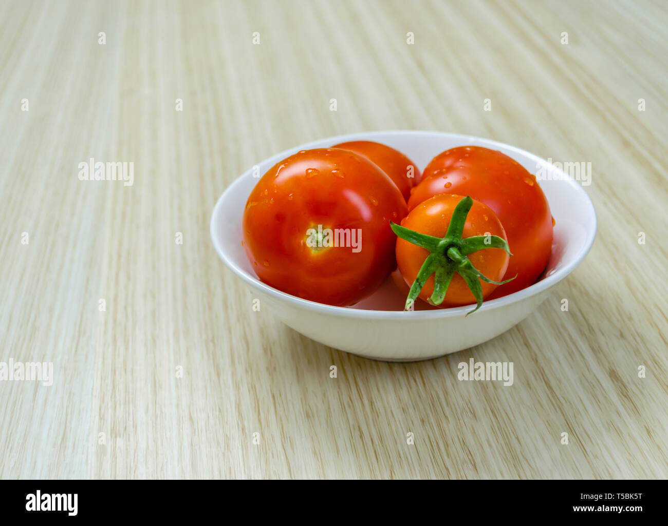 Frische, reife Tomaten in einem weißen Keramik Schüssel auf Holzboden. Nahaufnahme. Stockfoto