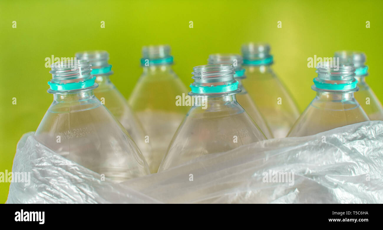 Engpässe in einer Packung mit 8 leeren und recycelbaren Kunststoff Flaschen mit Wasser, ohne Kappen, Sea Green Seal, in eine Plastiktüte, auf einem farbigen leuchtend gelben Stockfoto