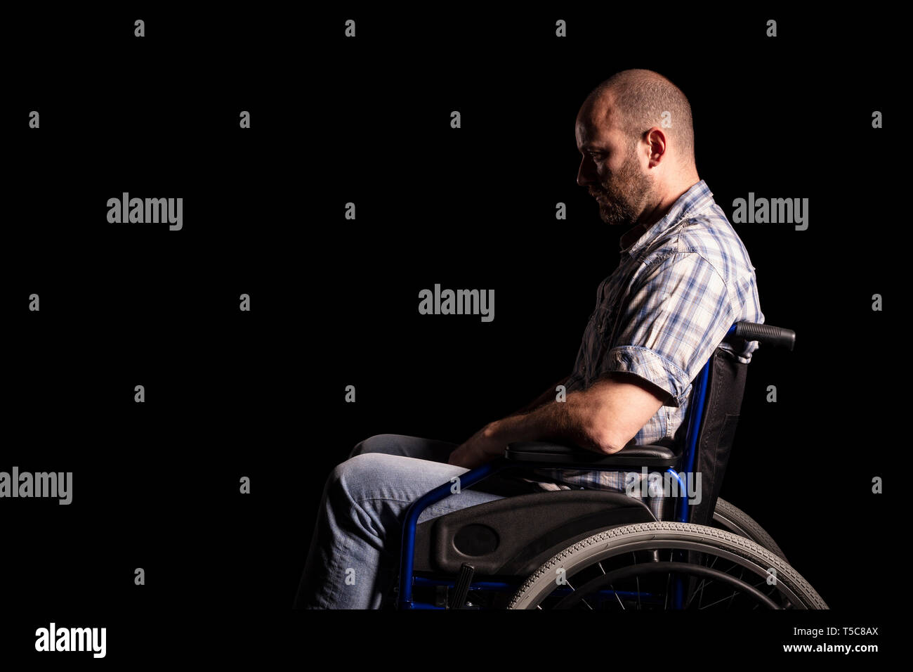 Portrait der kaukasischen Mann sitzt im Rollstuhl, traurige und nachdenkliche Ausdruck. Schwarzen Hintergrund. Konzept der Patienten- und körperlichen Behinderungen. Stockfoto