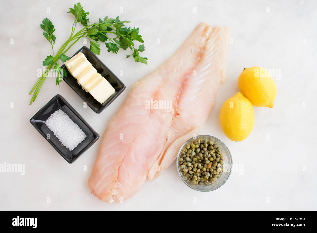 Zutaten: Großes, knochenloses Felchenfischfilet mit Kapern, Zitronen, Butter, Salz und Petersilie auf einem weißen Marmortisch Stockfoto