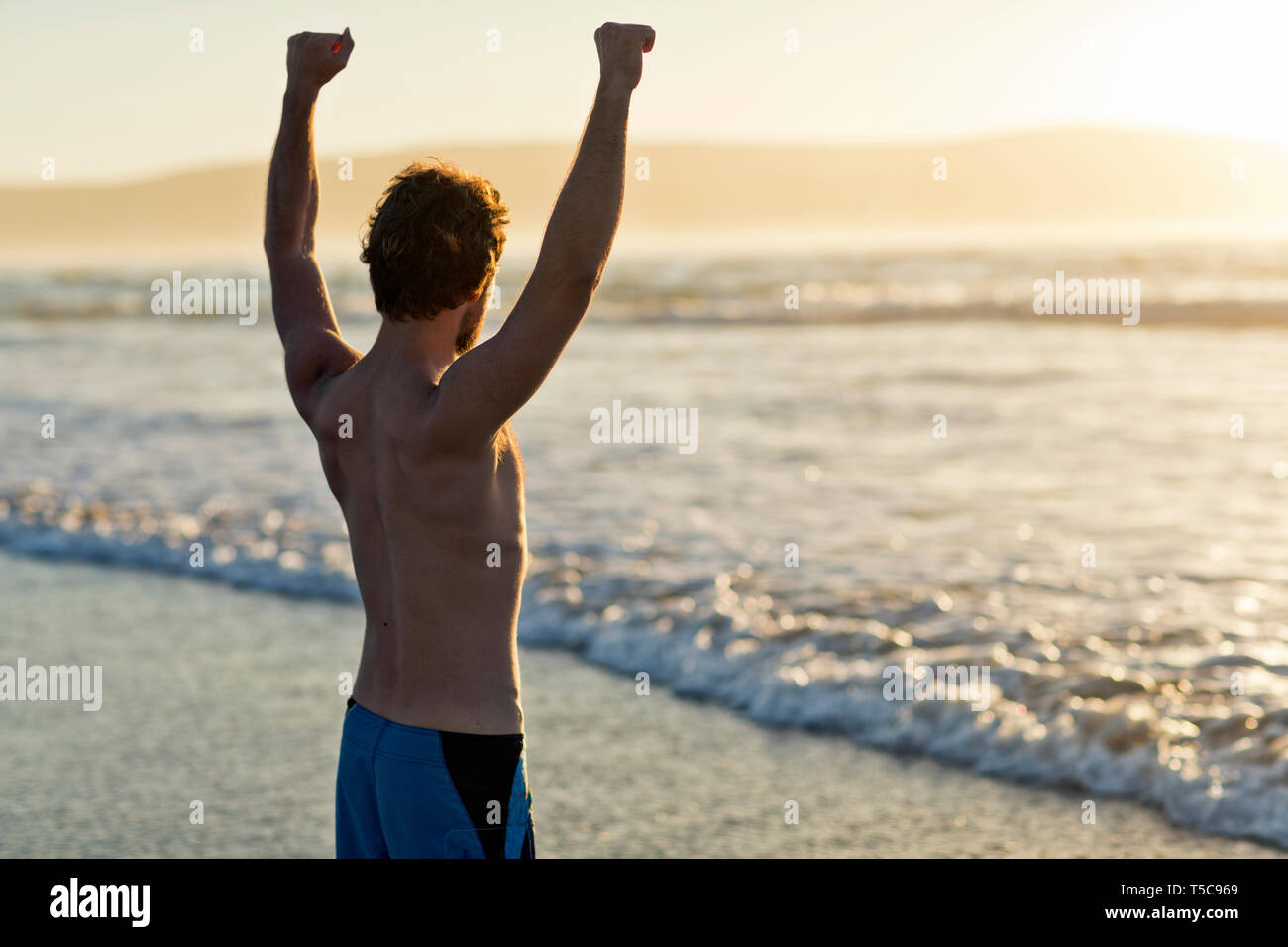 Mann mit Blick auf das Meer mit erhobenen Armen. Stockfoto