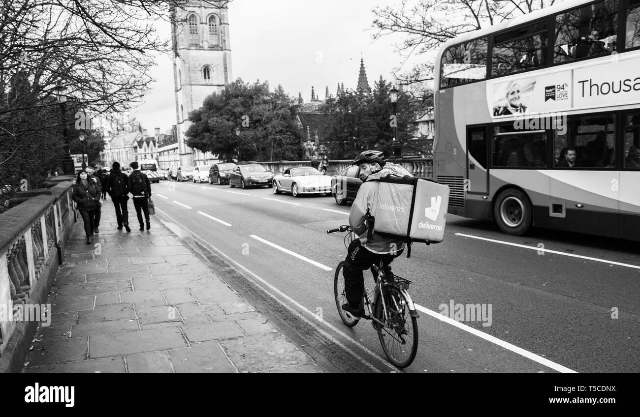 Oxford, Großbritannien - Mar 3, 3017: Schwarz und Weiß junge männliche Radfahrer Essen schnelle Client über Deliveroo App - auf dem Weg zur Arbeit schnell in die Universitätsstadt mit großen thermo Tasche mit Deliveroo logo Stockfoto