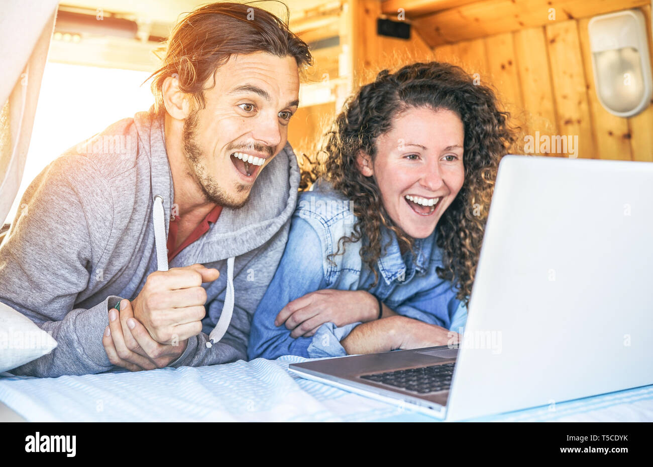 Glücklich der Mann und die Frau auf ihren Computer überrascht - Reisen Paar mit Laptop während ihrer Fahrt auf dem Vintage minivan mit Holz innen Stockfoto