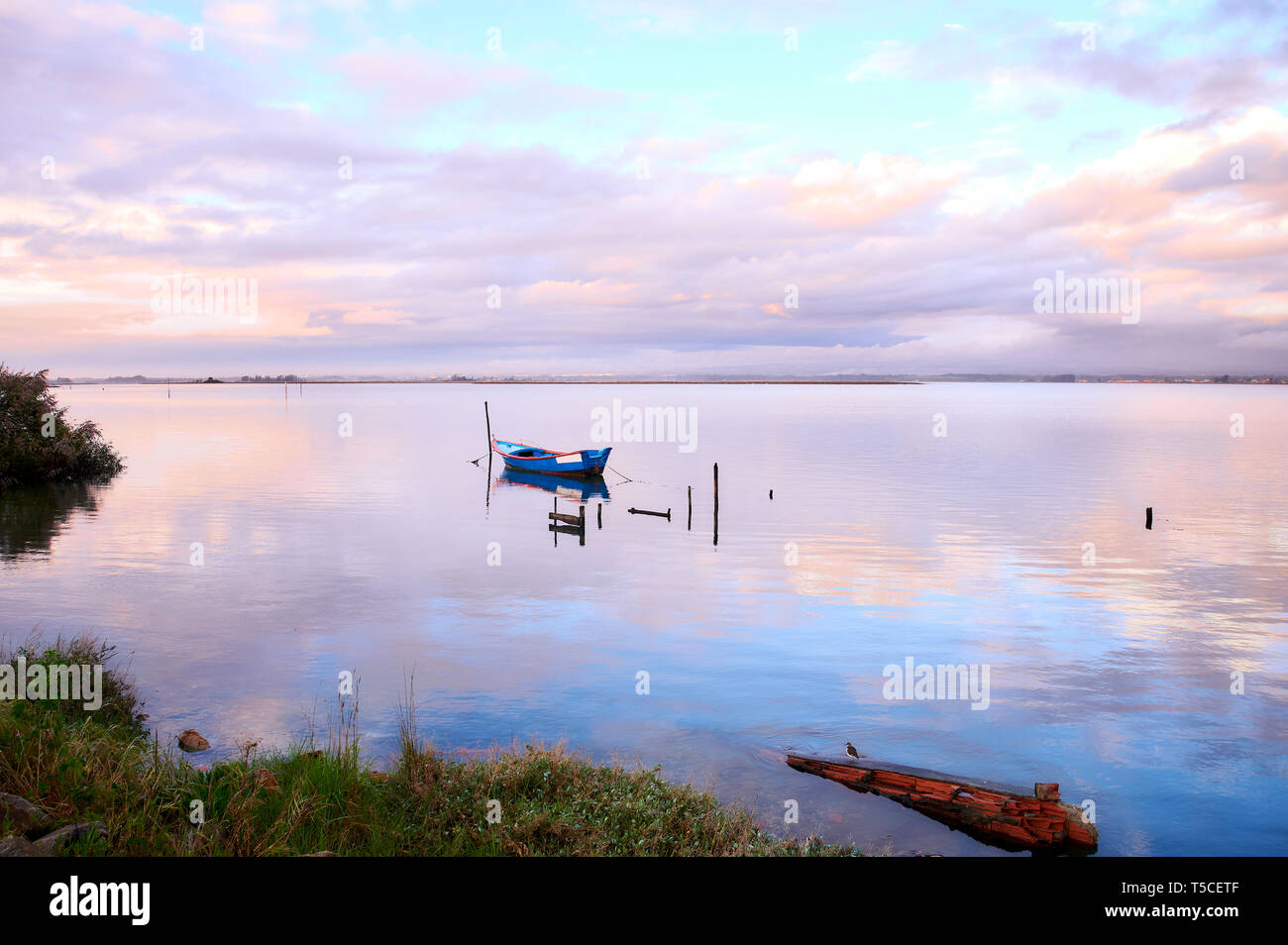 Einzelne Boot gebunden an einen Pfahl in der Mitte der Lagune von Aveiro in Sigulda. Die rosa und orange Sonnenuntergang winter Wolken am See Oberfläche reflektiert. Stockfoto