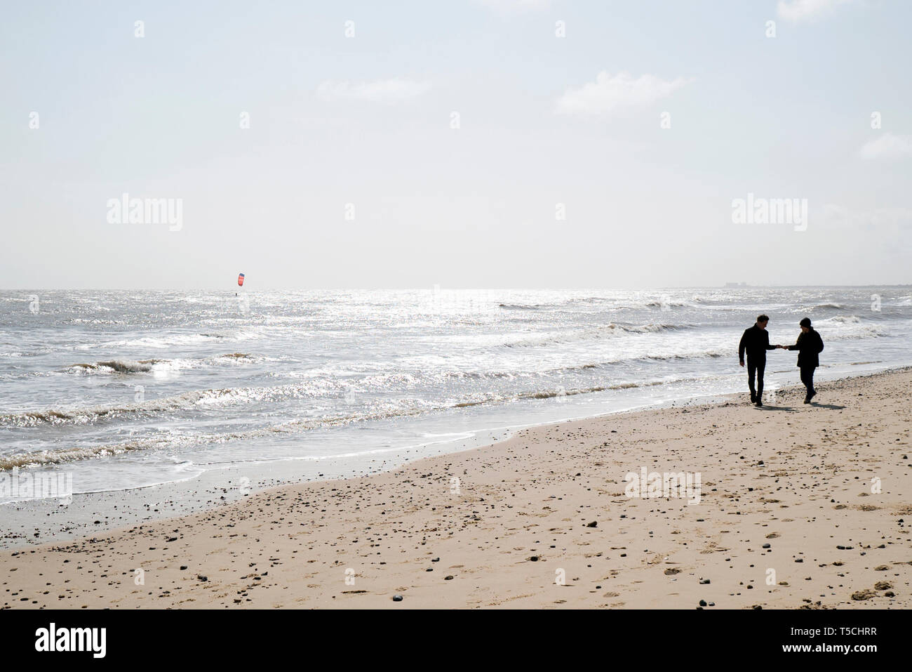 Ein paar Walking am Strand in Suffolk mit einem Kite Surfer in der Ferne Stockfoto
