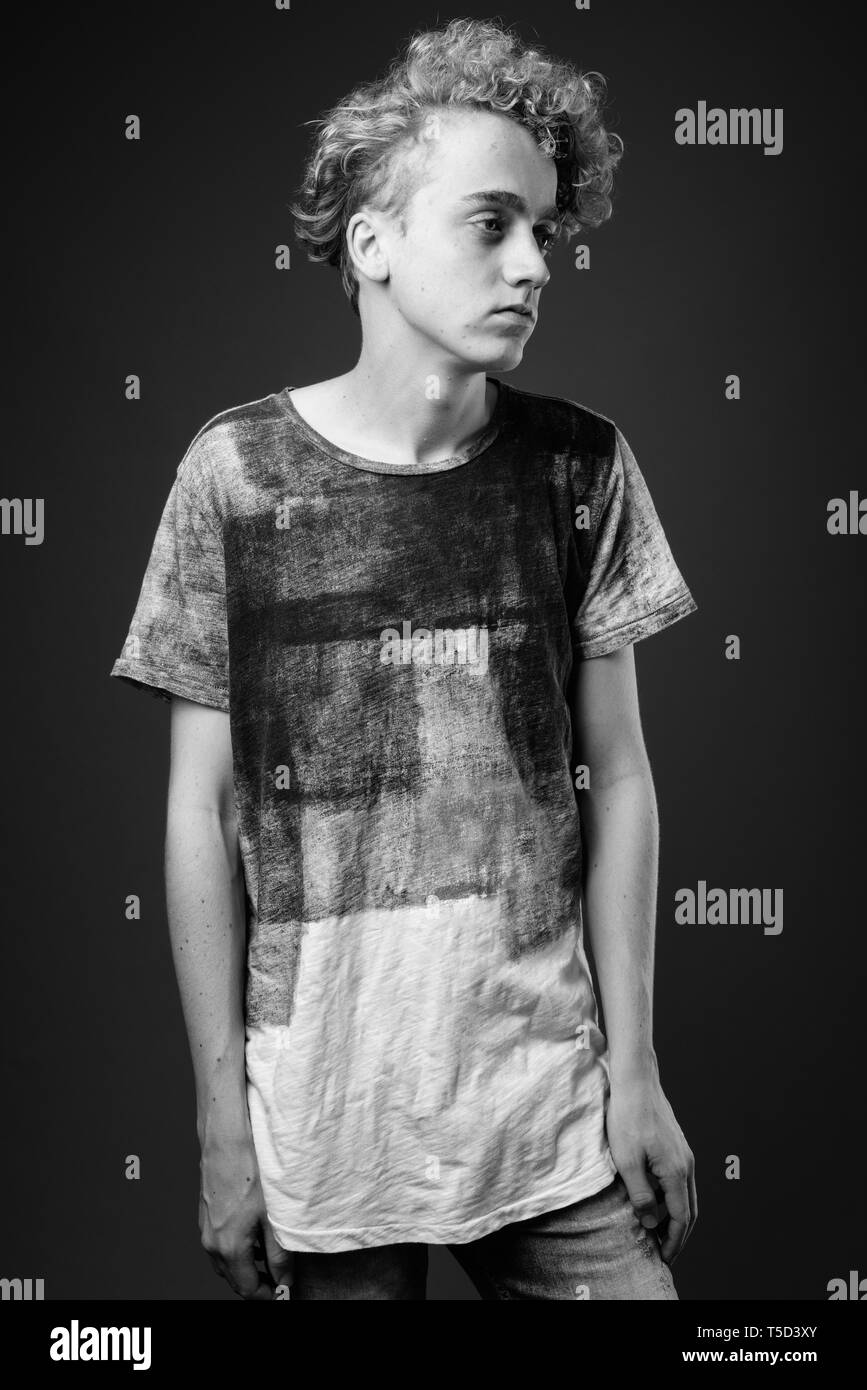 Skinny junger Mann mit lockigem Haar gegen grauen Hintergrund in blac Stockfoto