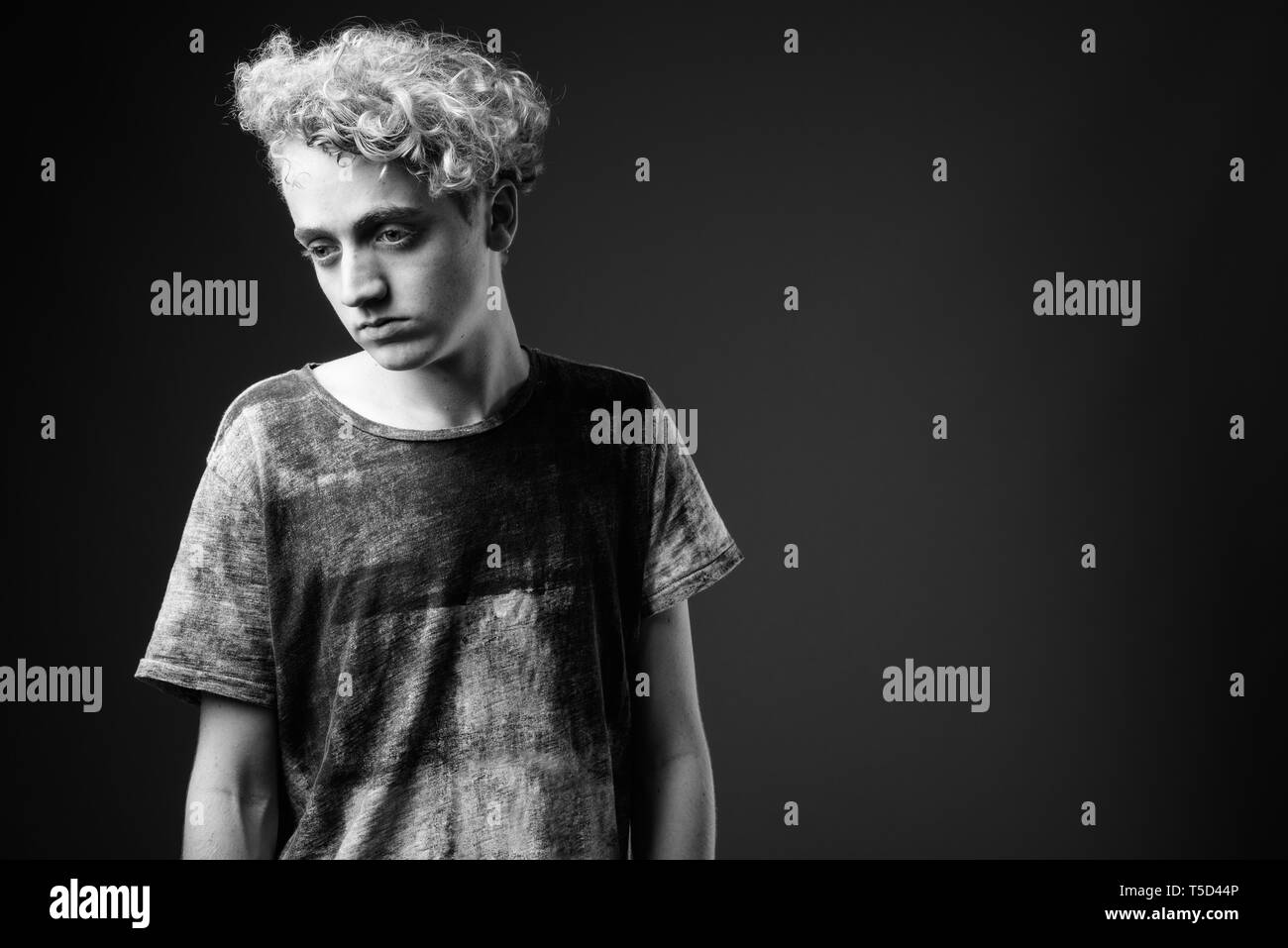 Skinny junger Mann mit lockigem Haar gegen grauen Hintergrund in blac Stockfoto