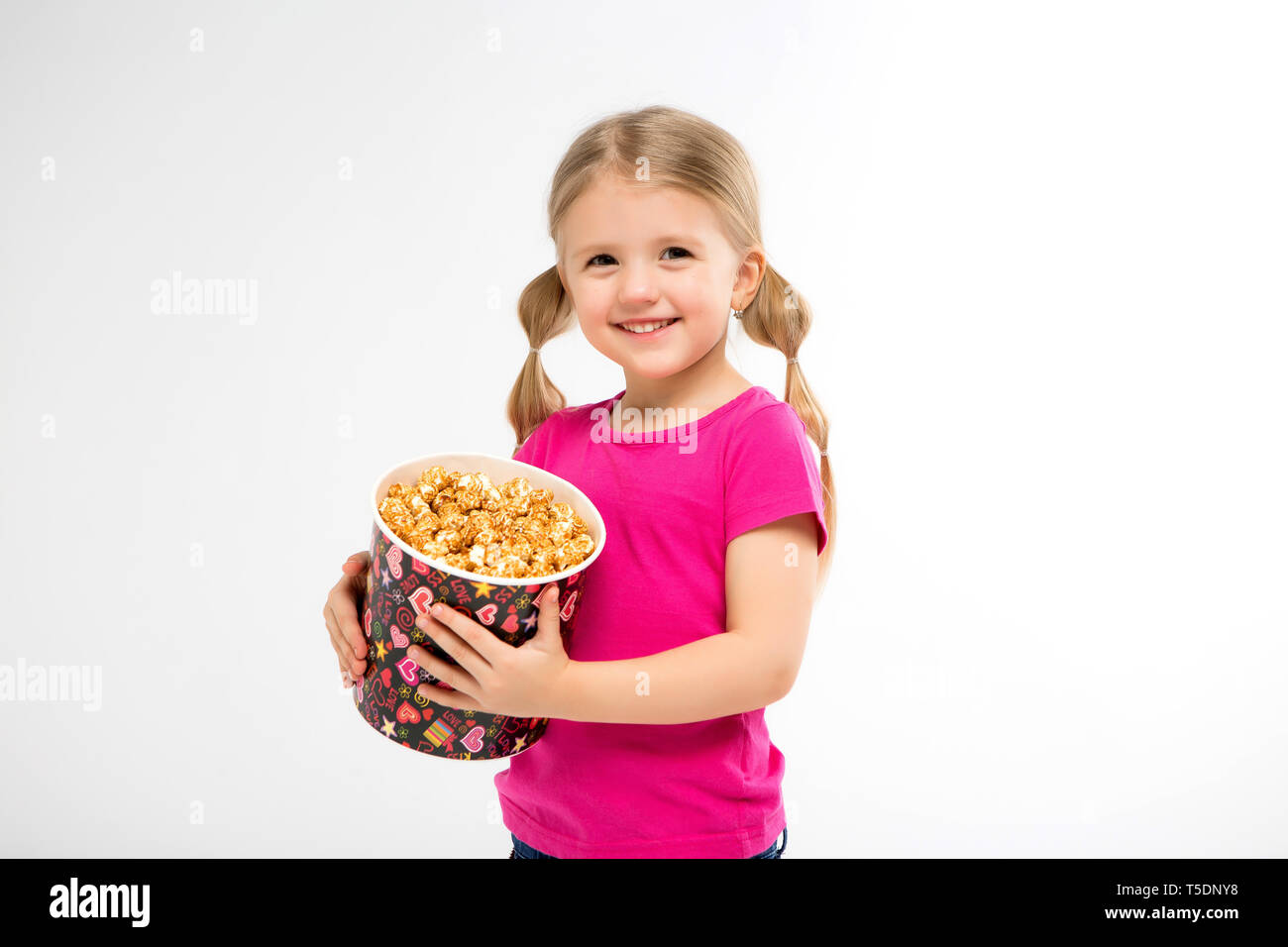 Baby Mädchen mit Popcorn auf weißem Hintergrund isolieren. kleinen niedlichen Baby Mädchen 3-4 Jahre alt mit einem Eimer Popcorn, Kinder Kindheit lifestyle Konzept. Stockfoto