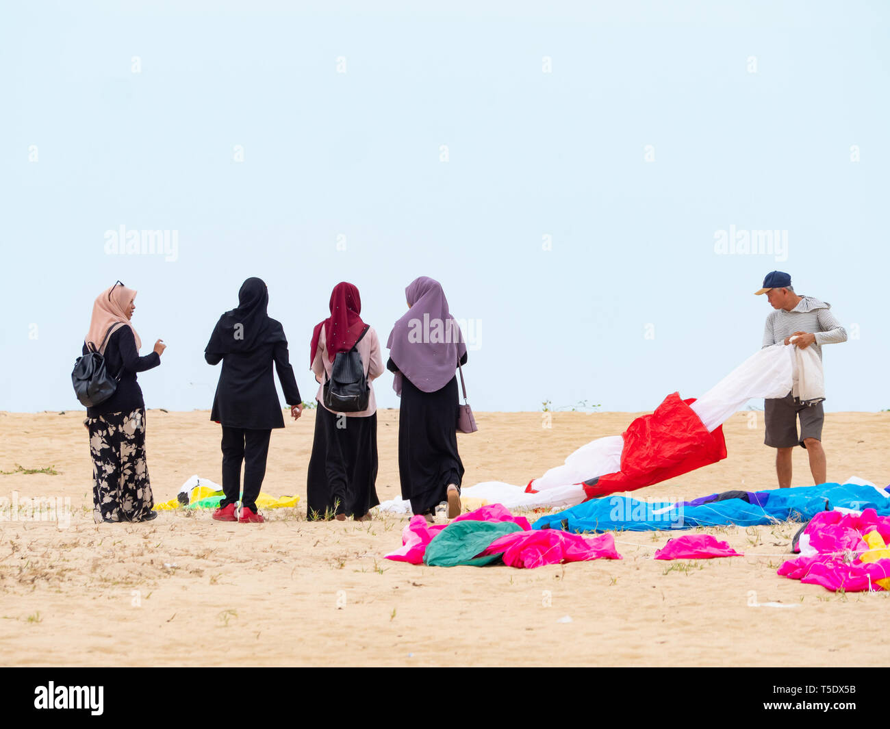 Vier muslimische Frauen tragen Kopftuch zu Fuß am Strand in der konservativen Kelantan Zustand von Malaysia. Neben ihnen ein Mann seine deflationiert weichen Ki vorbereiten Stockfoto