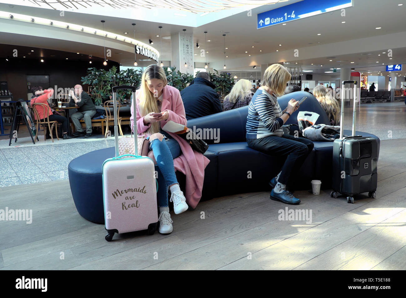 Menschen weibliche Reisende sitzen warten Flug Bristol Airport Departure Lounge Bank mit Gepäck auf Handy 2019 UK KATHY DEWITT Stockfoto