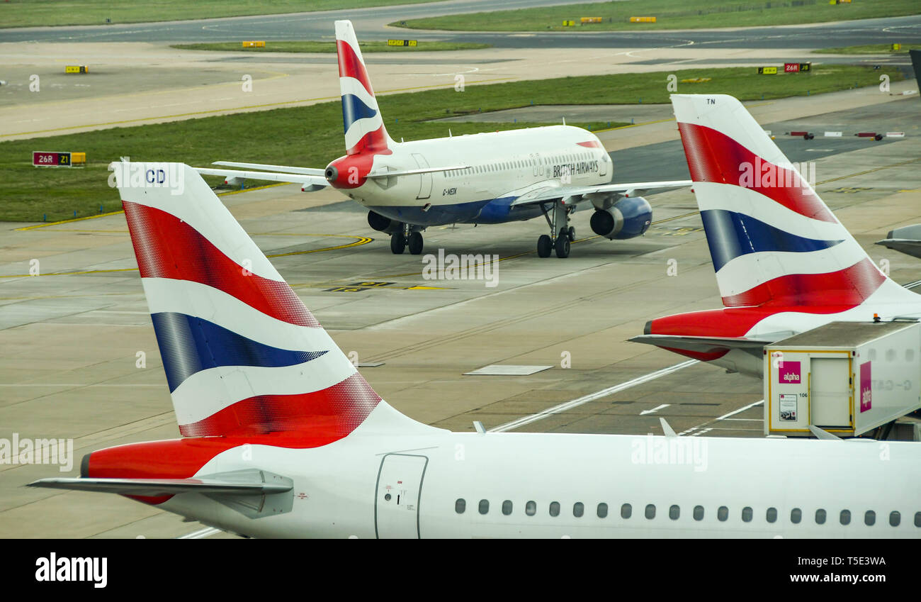 Der Flughafen London Gatwick, ENGLAND - April 2019: Schwanzflosse von zwei British Airways jets am Flughafen Gatwick mit einem anderen Flugzeug Rollen für den Weg in die Stockfoto