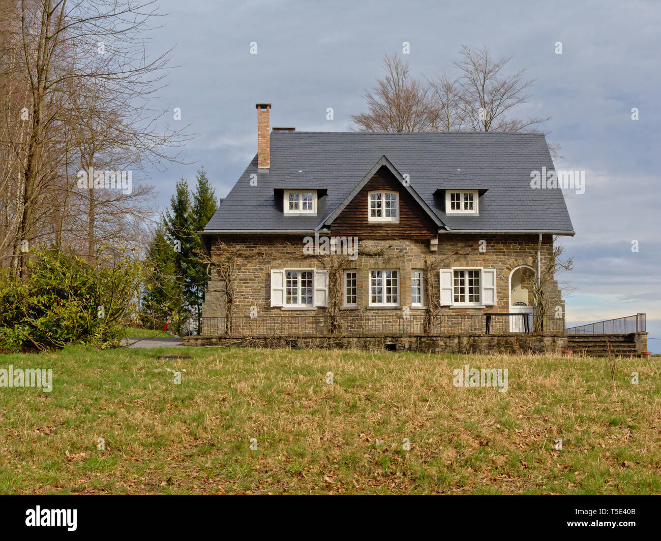 Traditionelle kleine Villa aus Naturstein unter einem bewölkten Himmel in Ardennen, Lüttich, Belgien Stockfoto