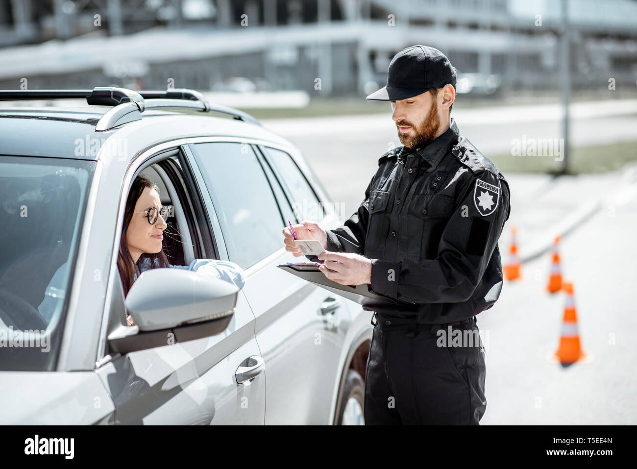 Polizist Dokumente prüfen einer jungen weiblichen Treiber stehen in der Nähe der Autos auf der Straße in der Stadt Stockfoto