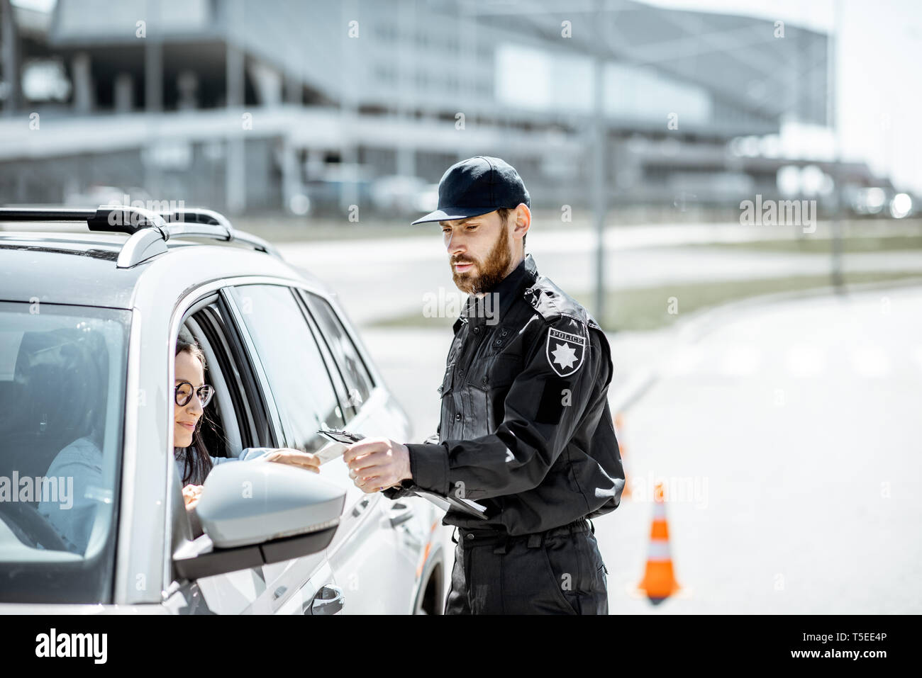 Polizist Dokumente prüfen einer jungen weiblichen Treiber stehen in der Nähe der Autos auf der Straße in der Stadt Stockfoto