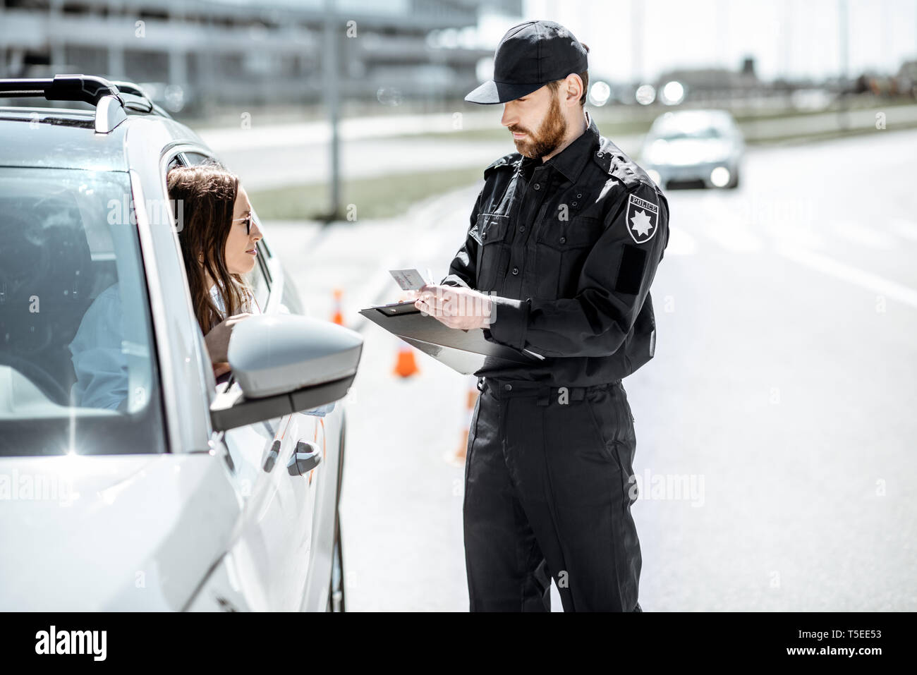 Polizist Dokumente prüfen einer jungen weiblichen Treiber stehen in der Nähe der Autos auf der Straße in der Stadt Stockfoto