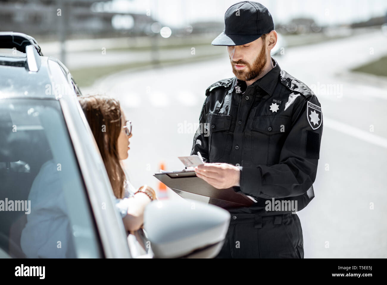 Polizist Dokumente prüfen einer jungen weiblichen Treiber stehen in der Nähe der Autos auf der Straße in der Stadt Stockfoto