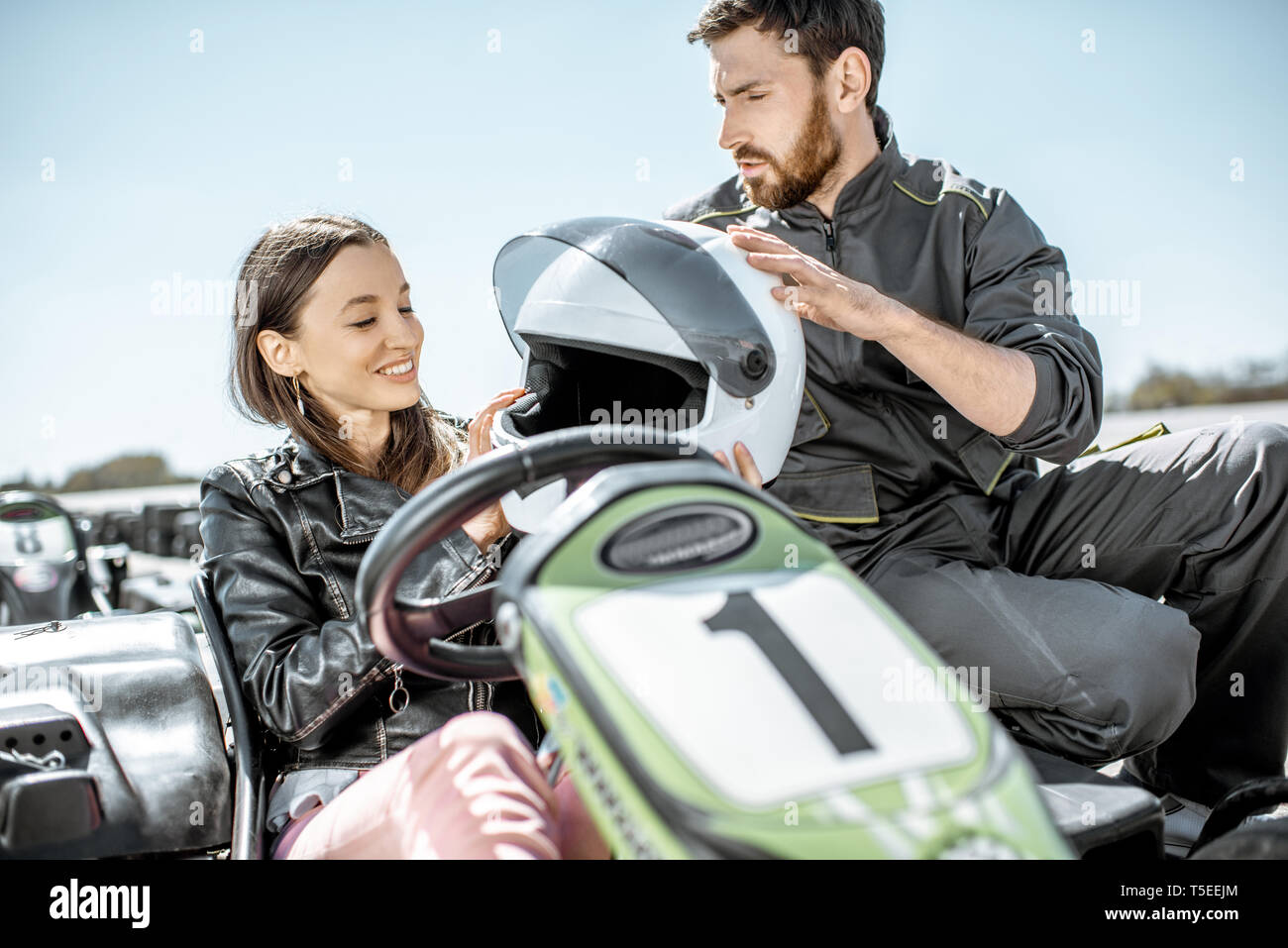 Kursleiter mit glücklichen jungen Frau Treiber durch das Tragen von schützender helm vor dem Rennen auf der Kartbahn im Freien Stockfoto