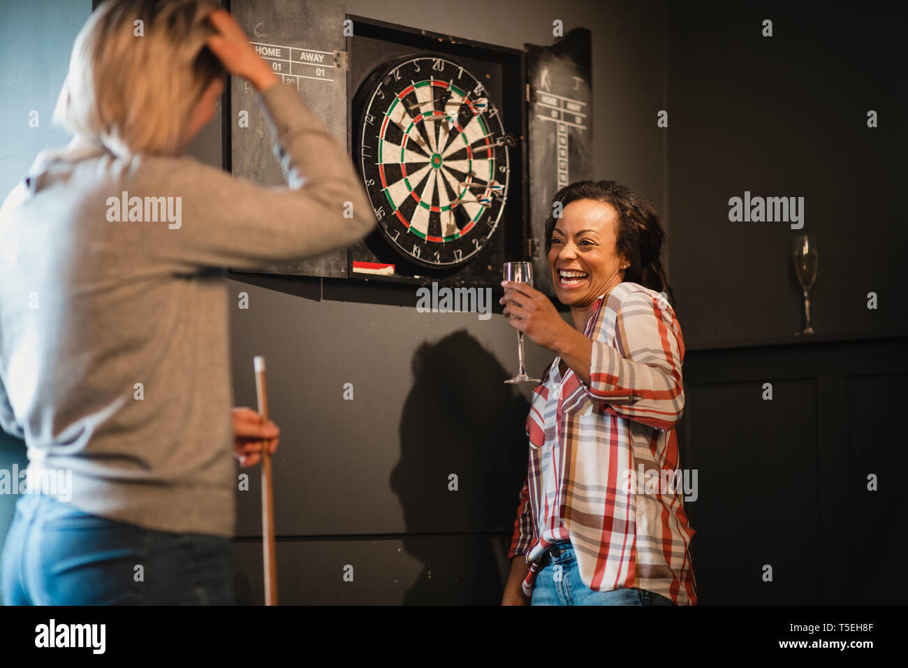 Zwei weibliche Freunde entspannen und Spaß haben. Sie stehen in einem Spielzimmer neben eine Dartscheibe, einen Drink. Stockfoto