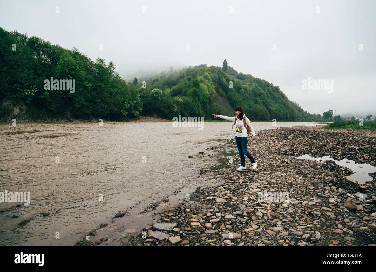 Touristische Mädchen in Jeans und weißen Sweatshirt mit orange Rucksack am Ufer des Berg River umgeben von Wald, genießen die Stille und Harmonie Stockfoto