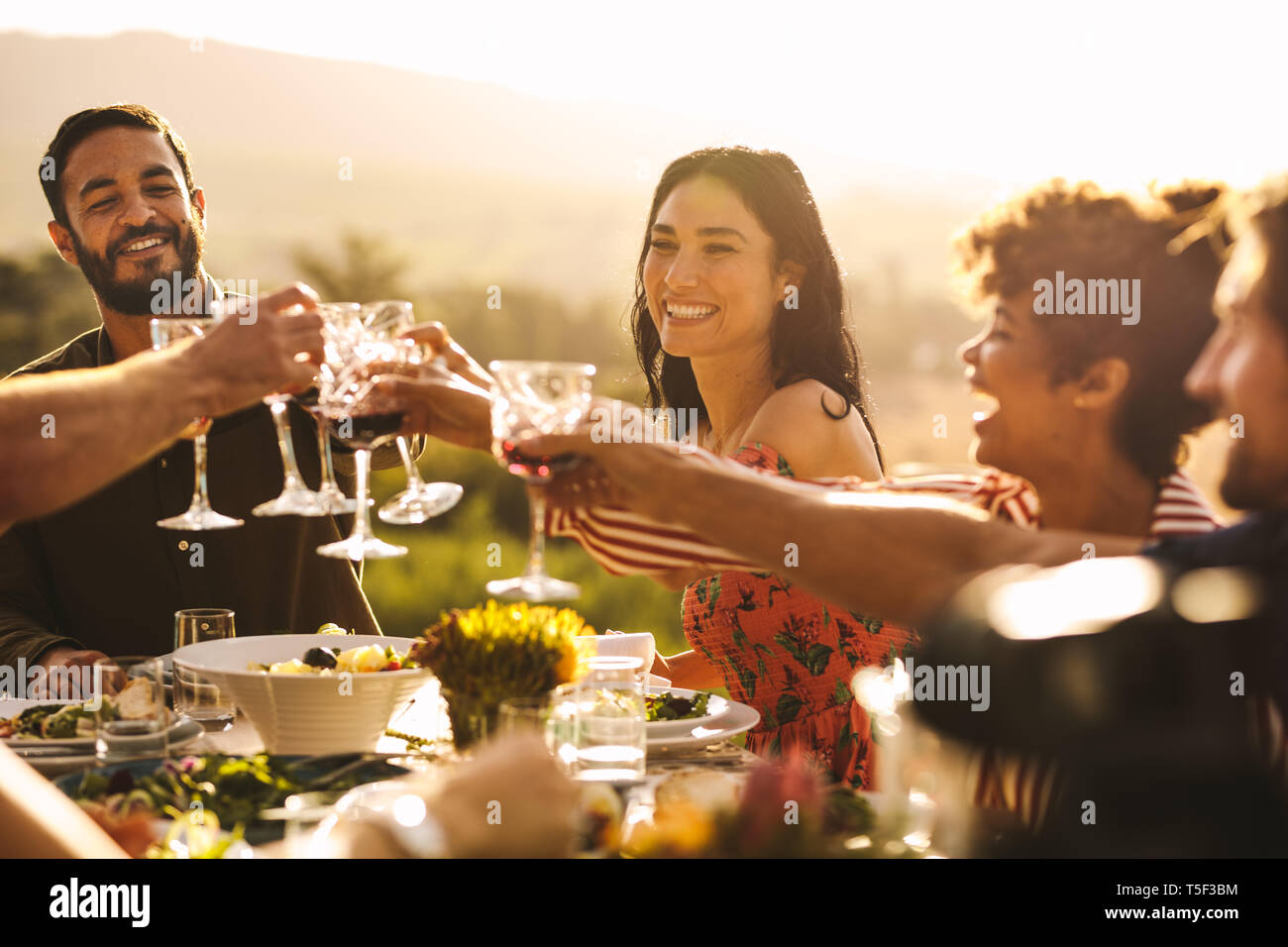 Eine Gruppe von Freunden einen Toast mit Getränken an der Partei. Junge Menschen an einem Tisch toasten Getränke und Abendessen zu genießen. Stockfoto