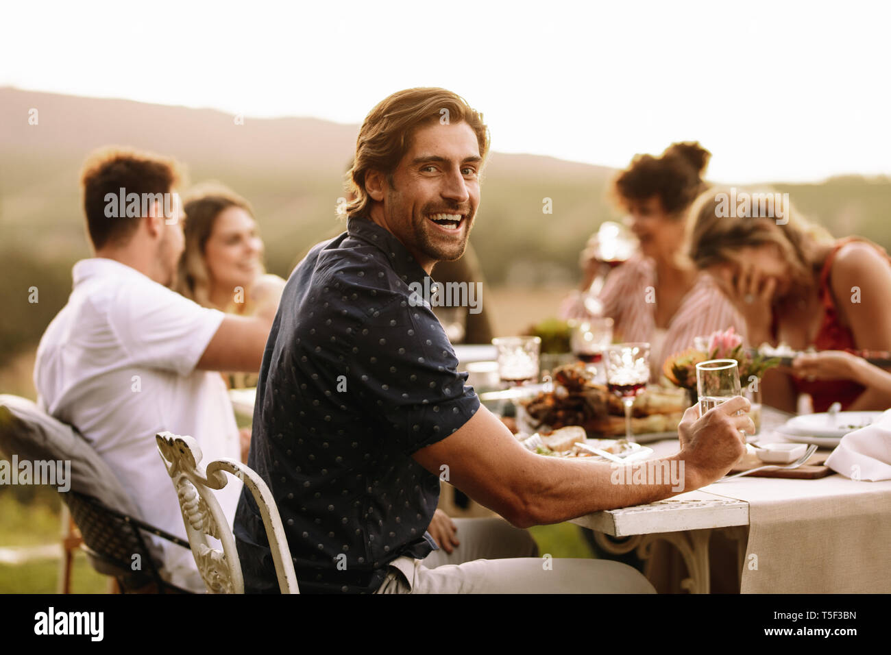 Schöner Mann Drinks mit Freunden sitzen beim Abendessen Partei. Jungen Kerl in Outdoor Party mit Freunden. Stockfoto