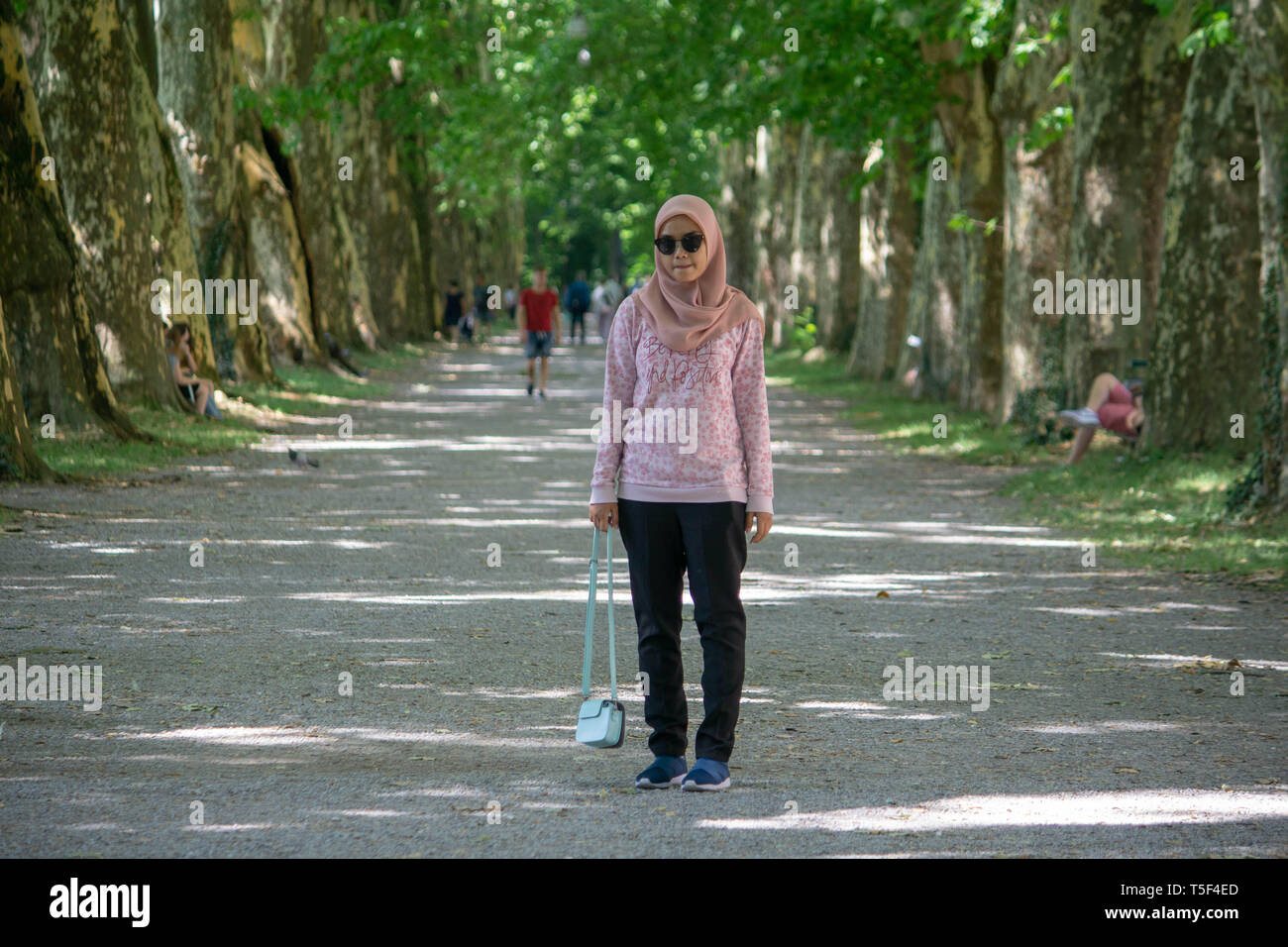 Tübingen/Deutschland - vom 29. Juli 2019: Asiatische moslemischen Mädchen Posen am grossen Garten. Mit rosa Hijab und Sonnenbrille, tragende schwarze Hose ein rosa Muster Swe Stockfoto