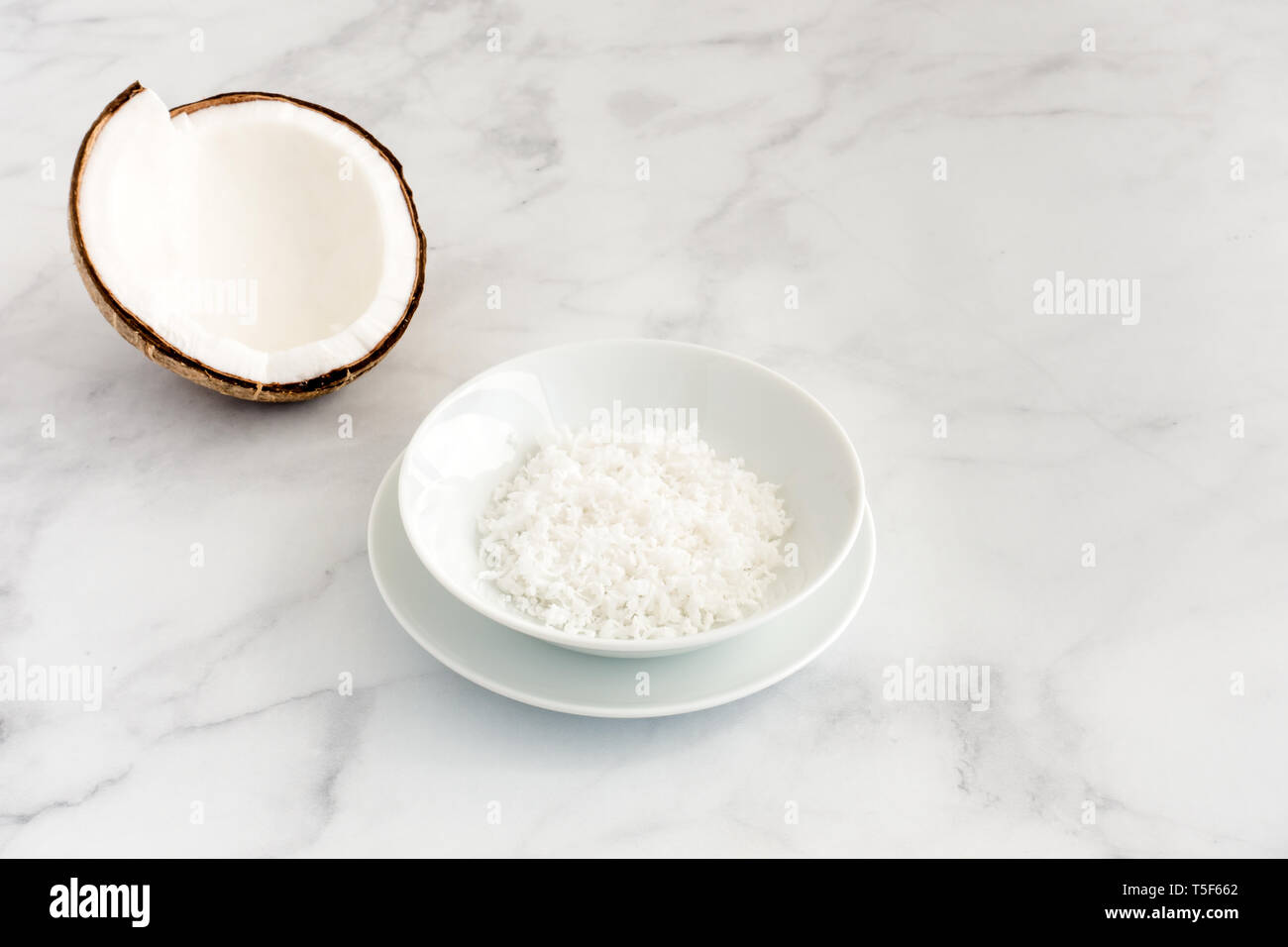 Coconut Hälfte und frisch geriebene Kokosraspeln in einer weißen Porzellan Schüssel auf weißem Hintergrund mit kopieren. Stockfoto