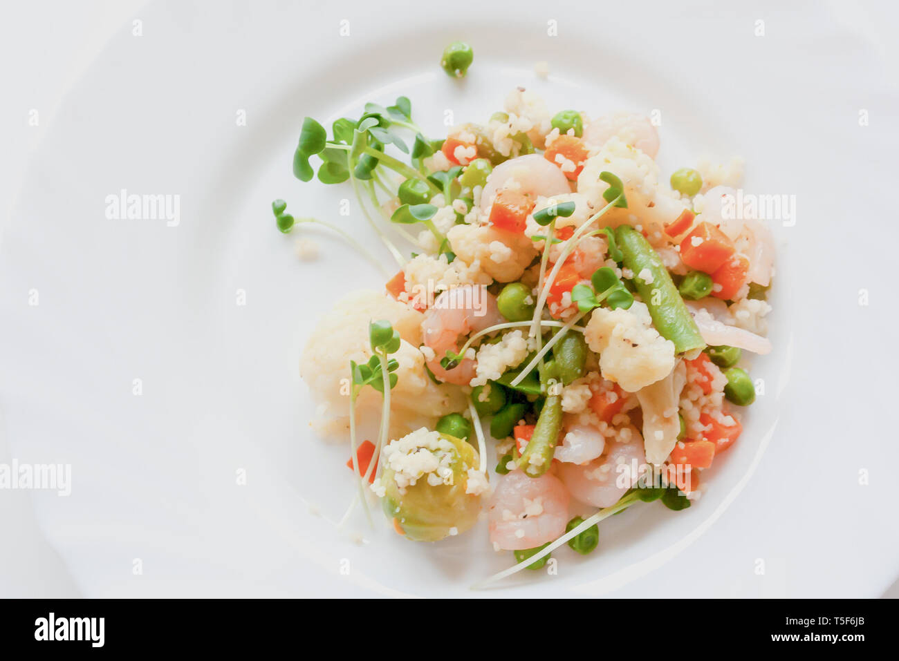 Couscous mit Gemüse, Garnelen und Radieschen auf einem weißen Teller Stockfoto