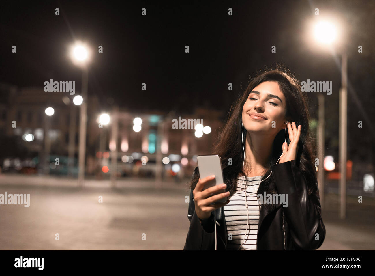 Junge Frau bei Musik im Kopfhörer, Wandern in Night city Stockfoto