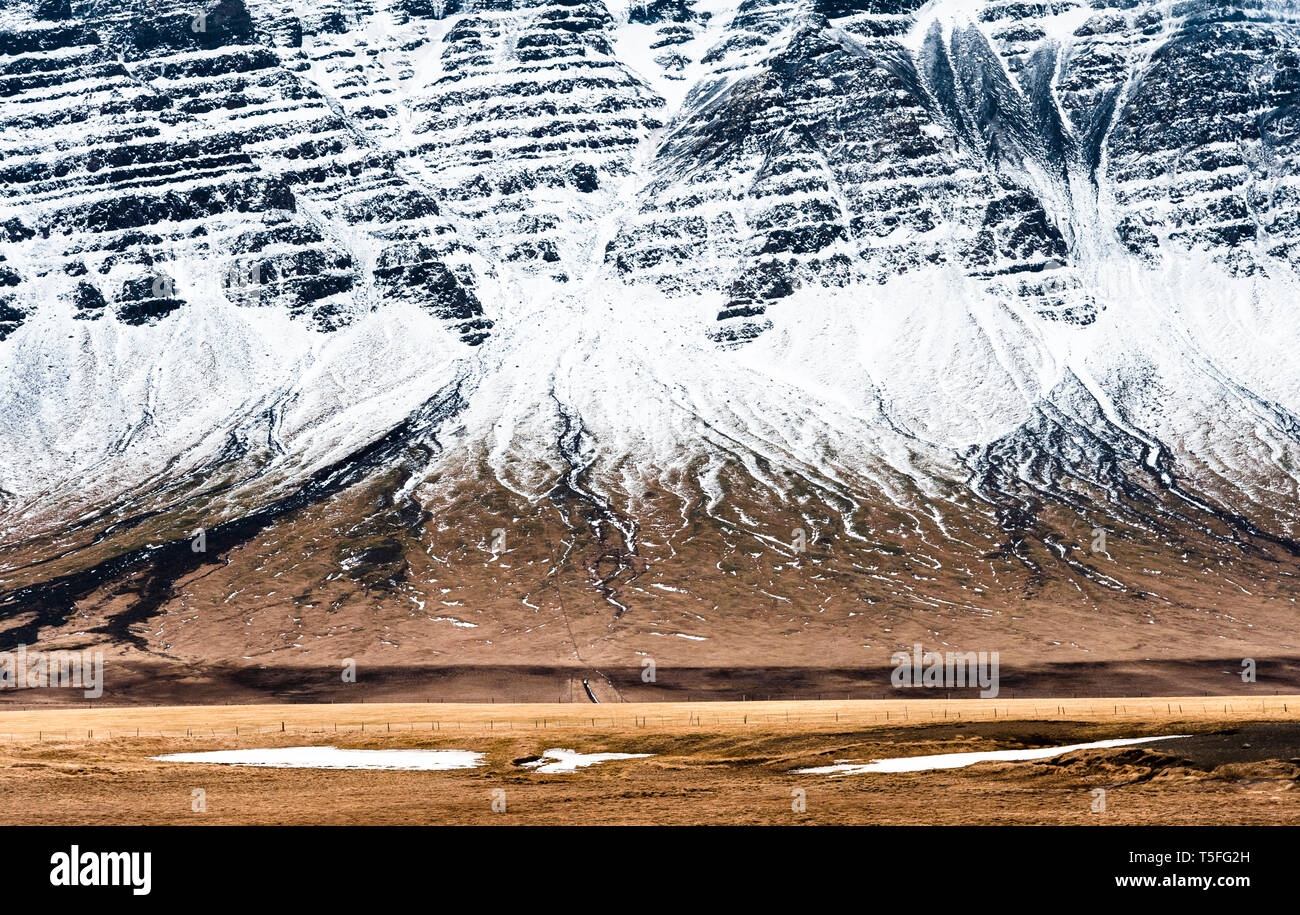 SW-Island Ende März am Ende des Winters. Die schneebedeckten Berge, die sich steil über Weideland steigende Stockfoto